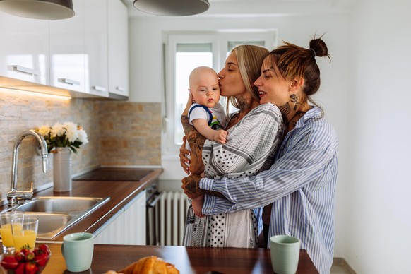 Same sex couple in pajamas hold their baby son and enjoying time spent together at home