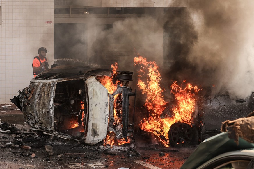 07.10.2023, Israel, Ashkelon: Nach einem Raketenangriff aus dem Gazastreifen versuchen Menschen, das Feuer auf Autos zu löschen. Nach massiven Angriffen aus dem palästinensischen Gazastreifen auf Isra ...