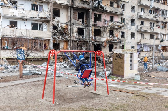February 25, 2022, Kyiv, Ukraine: A kid plays next to a damaged residential building following a Russian shelling attack as Russian forces launch full-scale invasion of Ukraine since February 24th. Ky ...