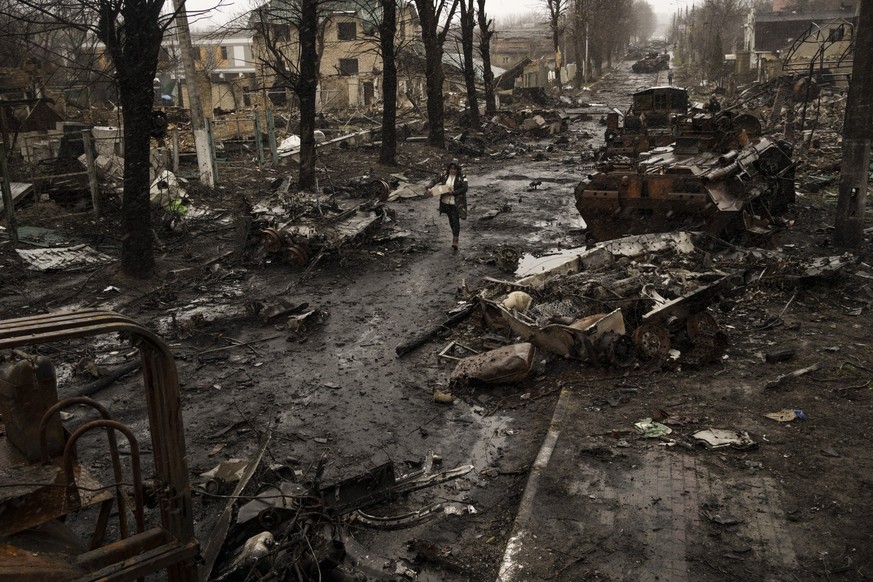 03.04.2022, Ukraine, Kiew: Eine Frau geht inmitten zerstörter russischer Panzer in Butscha am Stadtrand von Kiew, Ukraine, am 3. April 2022. Das Bild ist Teil einer Serie von Bildern von Fotografen de ...