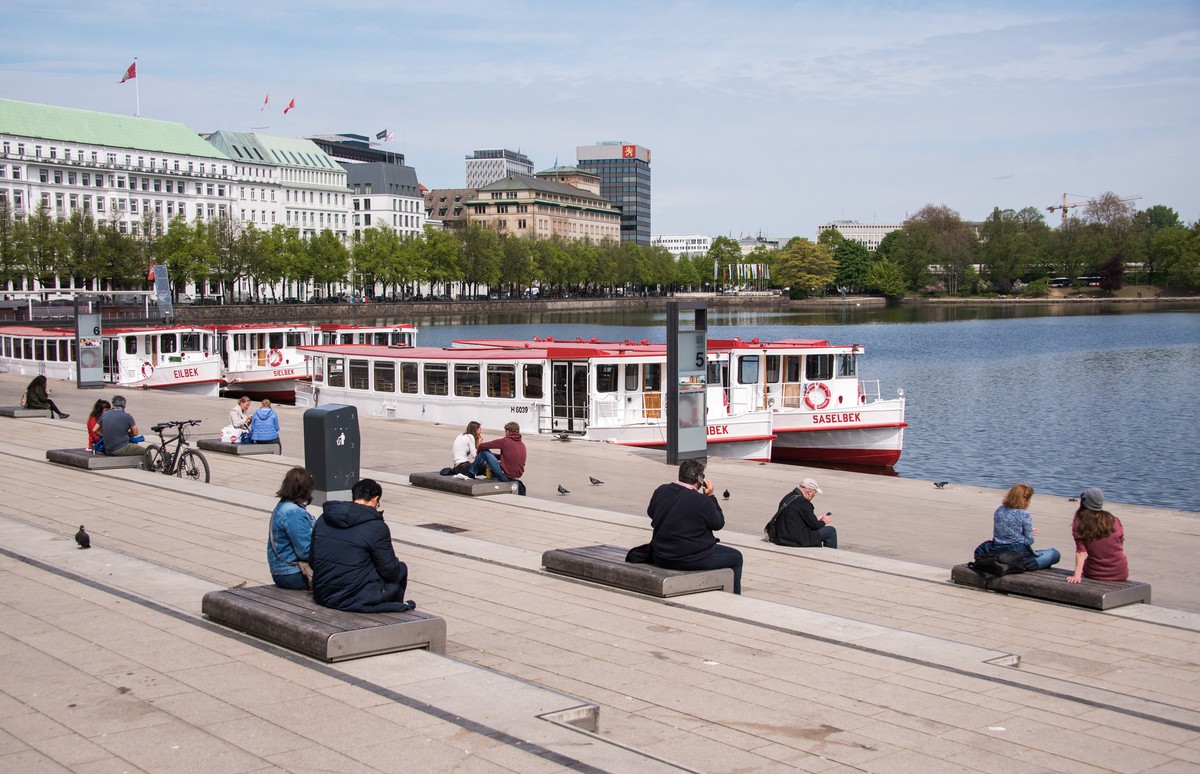 28.04.2020, Hamburg: Menschen sitzen mit Abstand zur Mittagszeit an der Alster am Jungfernstieg in der Sonne. Foto: Daniel Bockwoldt/dpa +++ dpa-Bildfunk +++