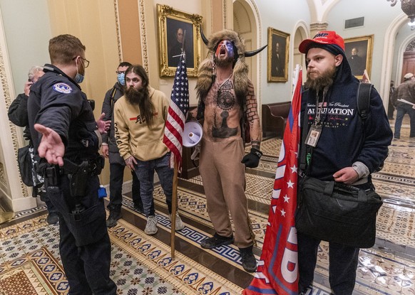 06.01.2021, USA, Washington: Unterst�tzer von US-Pr�sident Trump stehen vor Polizeien auf dem Gang vor der Senatskammer im Kapitol. (zu dpa &quot;Mann mit H�rner-Kopfschmuck nach Sturm aufs Kapitol fe ...