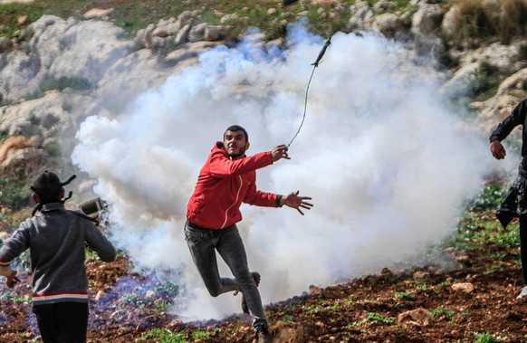 February 24, 2023, Nablus, West Bank, Palestine: A Palestinian demonstrator throws a tear gas canister after the Israeli soldiers fired it at him during the demonstration against Israeli settlements i ...