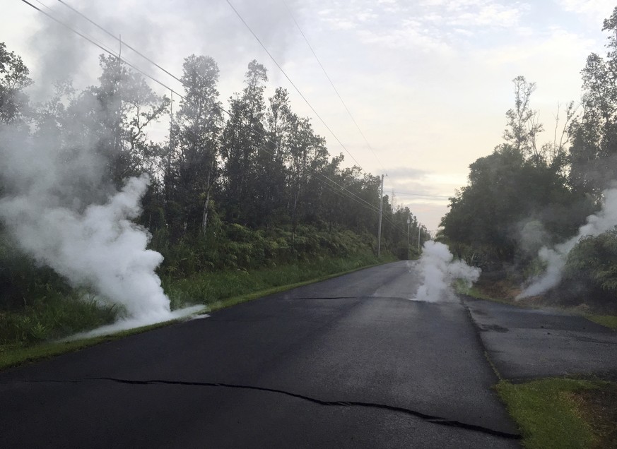 In this image released by the U.S. Geological Survey, steam rises from cracks in the road shortly before a fissure opened up on Kaupili Street in the Leilani Estates subdivision, Friday, May 4, 2018,  ...