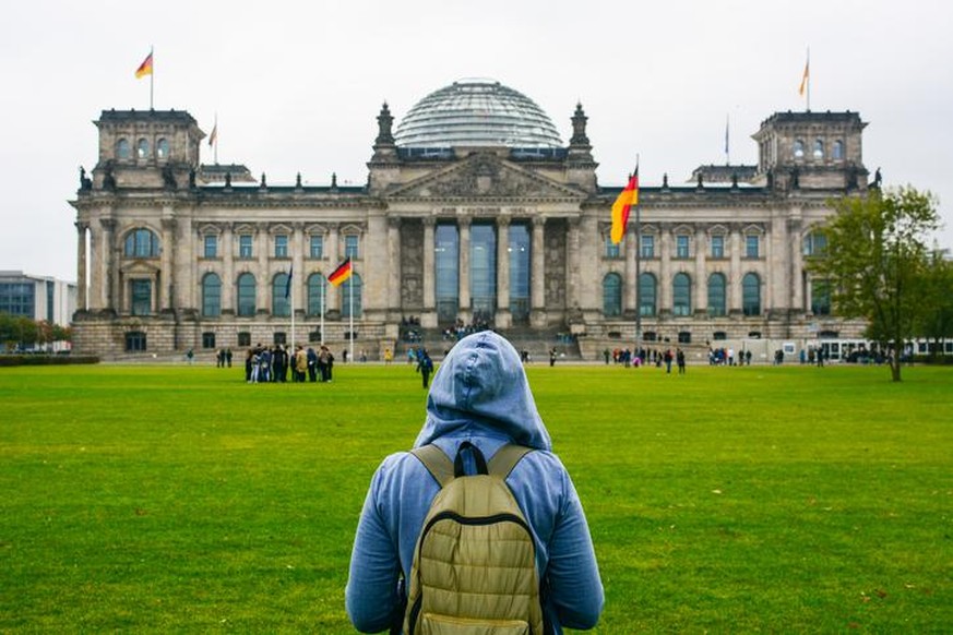 Young woman with backpack looking at Bundestag building in Berlin. Erasmus student, studying abroad and tourist concept.