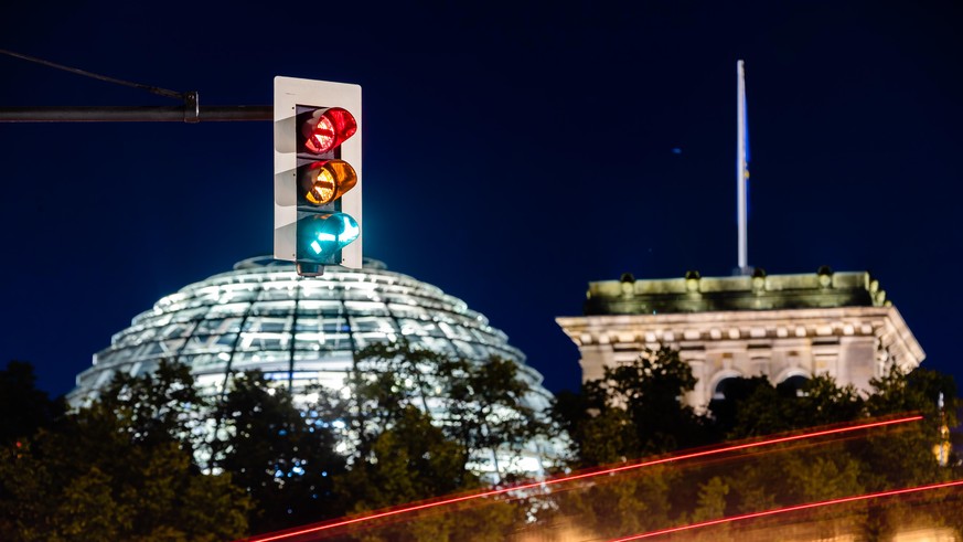 Eine Ampel vor dem Reichstagsgebäude leuchtet in einer Langzeitbelichtung in allen drei Phasen, wobei sich der Straßenverkehr als Leuchtspuren abzeichnet. (Aufnahme mit Langzeitbelichtung)