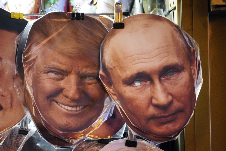 20.01.2025, Russland, St. Petersburg: Gesichtsmasken, die den designierten US-Präsidenten Donald Trump und den russischen Präsidenten Wladimir Putin darstellen, hängen neben anderen in einem Souvenirl ...