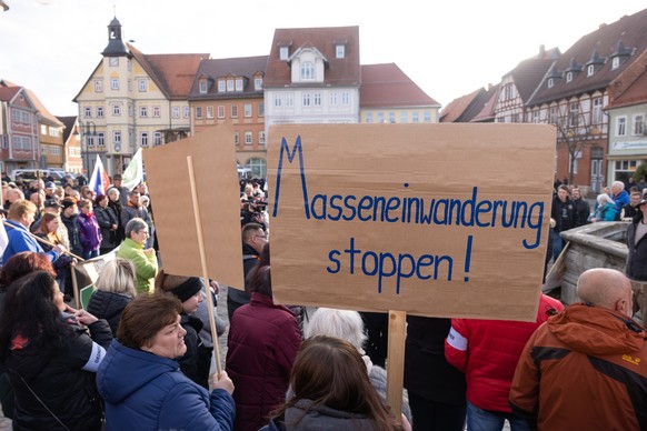 26.04.2023, Thüringen, Schleusingen: Menschen demonstrieren mit Transparenten und Fahnen gegen ein geplantes Flüchtlingsheim in einem einstigen Krankenhaus. In dem seit kurzem leerstehenden Gebäude so ...