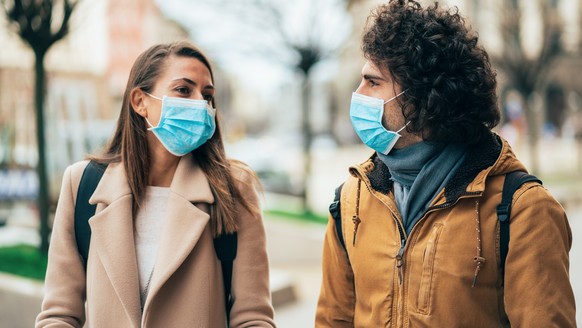 Young couple meet in quarantine outside on the city street wearing face protective mask to prevent Coronavirus and anti-smog