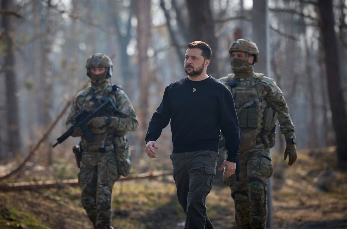 ARCHIV - 21.03.2023, Ukraine, Moschun: Wolodymyr Selenskyj (M), Präsident der Ukraine, erweist den Soldaten und Freiwilligen, die bei der Verteidigung der Hauptstadt während der ersten russischen Inva ...