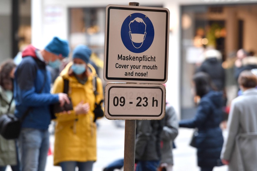 Personen mit Mundschutz,Maske gehen an einem Schild Maskenpflicht Cover your mouth and nose von 9-23 Uhr vorbei. Maskenpflicht in Fussgaengerzonen und oeffentlichen Plaetzen in Muenchen am 15.10.2020. ...