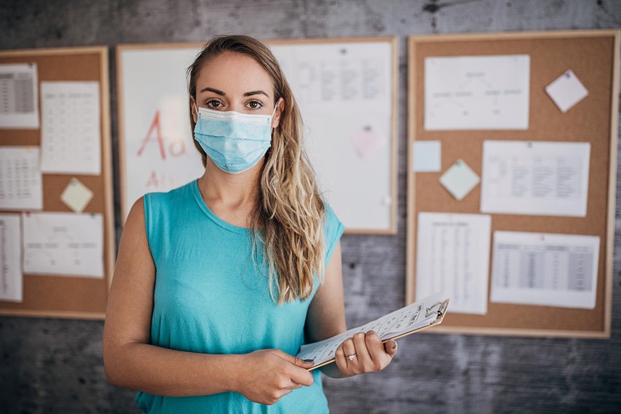 Back to school with preventive measures to stop spreading coronavirus. Female language teacher wearing protective face mask during class.