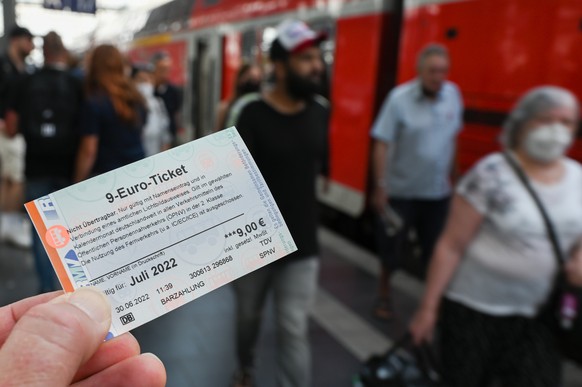 ARCHIV - 30.06.2022, Hessen, Frankfurt/Main: Ein 9-Euro-Ticket f�r Juli 2022 wird am Hauptbahnhof hochgehalten, w�hrend Zugreisende aus einer Regionalbahn aussteigen. (zu dpa: Inflation weiter �ber 7 ...