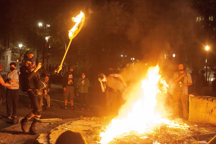 July 19, 2020, Portland, Oregon, U.S: July 18, 2020 A protester dances around a fire set by protesters while burning a peace sign near the Federal Courthouse in Portland, Oregon during another night o ...