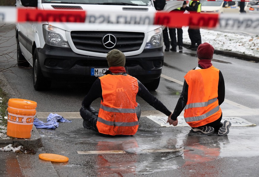 dpatopbilder - 14.12.2022, Bayern, München: Zwei Klimaaktivisten nehmen an einer Protestaktion der Gruppe &quot;Letzte Generation&quot; teil, indem sie versuchen sich auf einer Strasse trotz Nieselreg ...