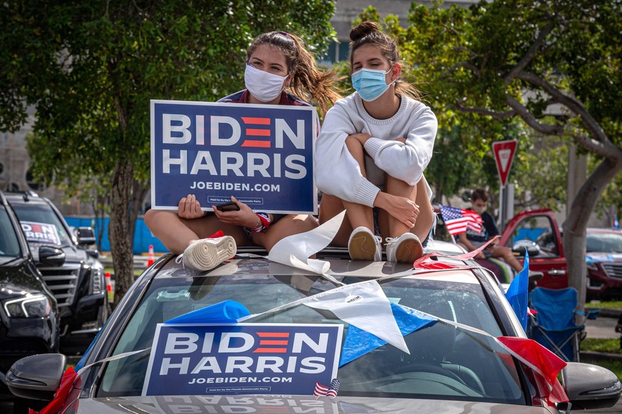 Two young people hold a banner in support of the Biden Harris formula while listening to the speech of former US President Barack Obama sitting on the roof of a car, during an act in support of the De ...