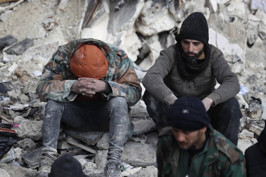 07.02.2023, Syrien, Aleppo: Menschen sitzen auf den Trümmern eingestürzter Gebäude. Die Zahl der Toten im Erdbebengebiet an der türkisch-syrischen Grenze steigt - und nach wie vor werden viele Mensche ...