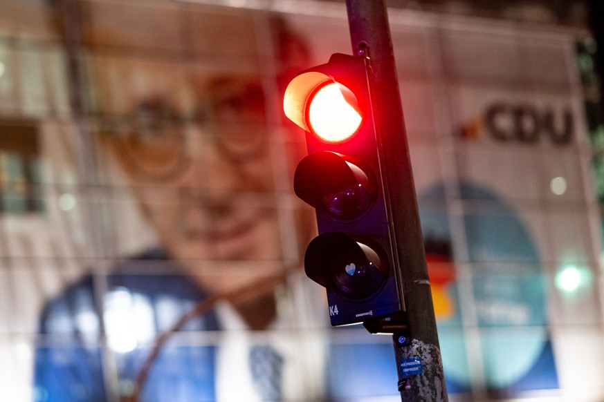 29.01.2025, Berlin: Eine Rote Ampel leuchtet am Rande der Demo «Brandmauer statt Brandstiftung» von Amnesty International, Seebrücke und anderen Organisationen vor einem Portrait von Merz (CDU), Spitz ...