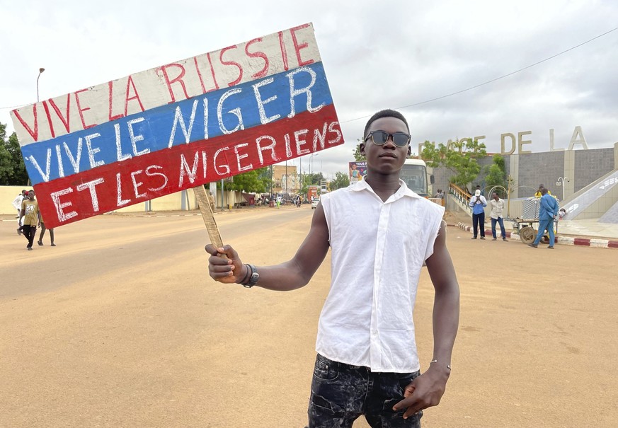03.08.2023, Niger, Niamey: Ein Anhänger von Nigers regierender Junta hält ein Plakat in den Farben der russischen Flagge mit der Aufschrift &quot;Lang lebe Russland, lang lebe der Niger und die Nigeri ...