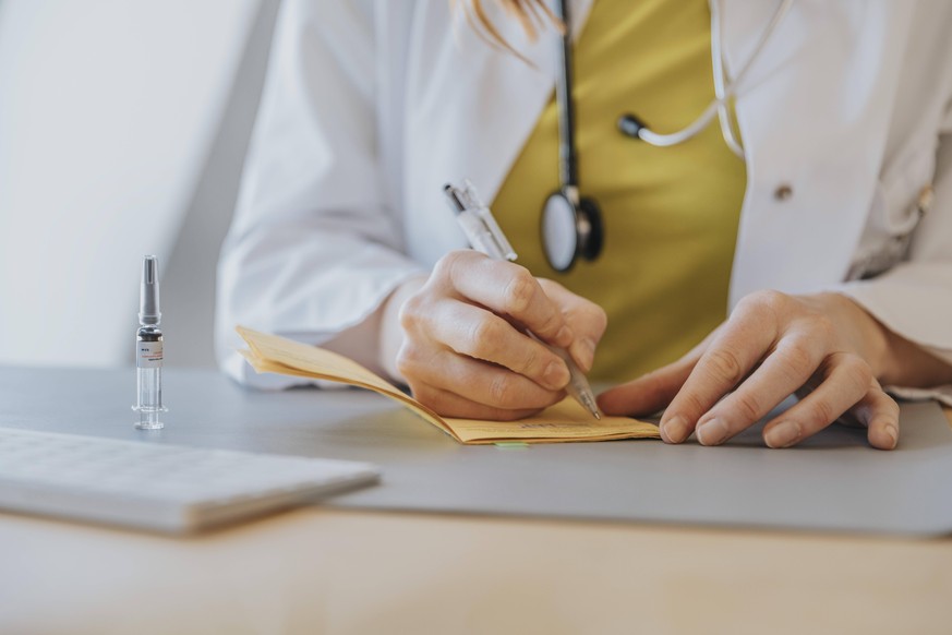 Doctor signing vaccination certificate while sitting by desk in office model released Symbolfoto property released MFF07419