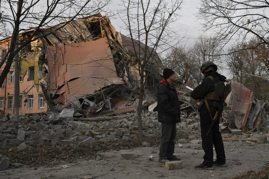 A police officer talks with a local resident as they stand in front of a school that was damaged in Russian shelling in Kramatorsk, Ukraine, Thursday, Dec. 22, 2022. (AP Photo/Andriy Andriyenko)
