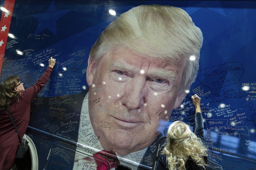 Supporters of Republican presidential candidate former President Donald Trump sign a campaign bus during the Conservative Political Action Conference, CPAC 2024, at the National Harbor in Oxon Hill, M ...