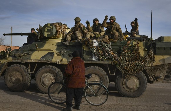 02.12.2022, Ukraine, Saritschne: Ukrainische Soldaten winken einem Anwohner zu, während sie auf einem Militärfahrzeug vorbeifahren. Foto: Andriy Andriyenko/AP/dpa +++ dpa-Bildfunk +++