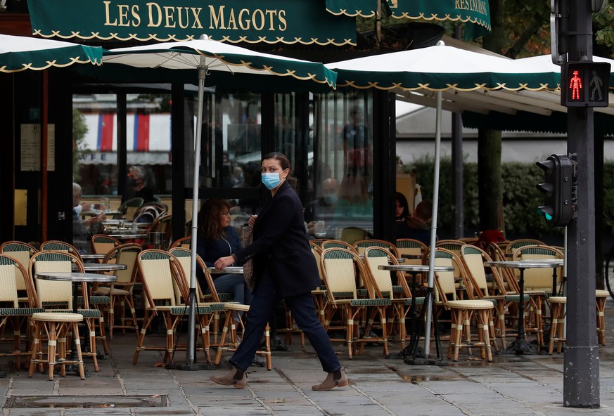 A woman wearing a protective face mask walks past the cafe and restaurant Les Deux Magots in Paris, during the announcement of new Covid restrictions by Paris authorities as the coronavirus disease (C ...