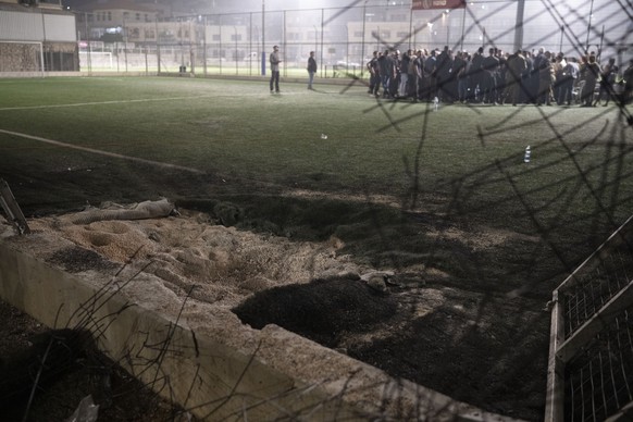 27.07.2024, Israel, Madschd al-Schams: Anwohner versammeln sich mit den Behörden auf einem Fußballplatz in der Stadt Madschd al-Schams in den von Israel besetzten Golanhöhen, der von einer Rakete getr ...