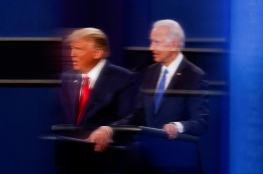 FILE PHOTO: U.S. President Donald Trump and Democratic presidential nominee Joe Biden are reflected in the plexiglass protecting a TV camera operator from coronavirus as they participate in their seco ...