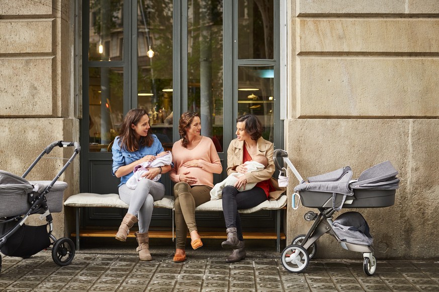 Expectant sitting amidst friends carrying babies outside restaurant