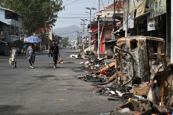 People walk past a burnt vehicle and rubble on a street in Churachandpur in violence hit areas of northeastern Indian state of Manipur on May 9, 2023. More than 50 people have been killed in the hilly ...