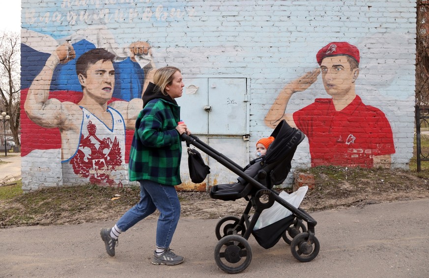 KRASNOGORSK, RUSSIA - APRIL 10: (RUSSIA OUT) A woman pushes her baby carriage walking past to a patriotic graffiti with Russian flag on April 10, 2023 in Moscow&#039;s suburb of Krasnogorsk, Russia. R ...