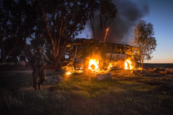 An Israeli soldier stands near a burning bus after it was hit by a mortar shell fired from Gaza near the Israel Gaza border, Monday, Nov. 12, 2018. Israel's military says it is prepared to step up its ...
