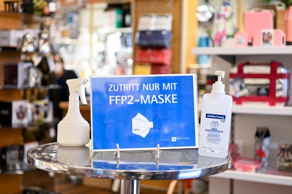 Ein Hinweisschild mit der Aufschrift &quot;Zutritt nur mit FFP2-Maske&quot; steht zusammen mit Desinfektionsmittel in einem Haushaltswarenladen. Die Ministerpräsidentenkonferenz hat über das weitere V ...