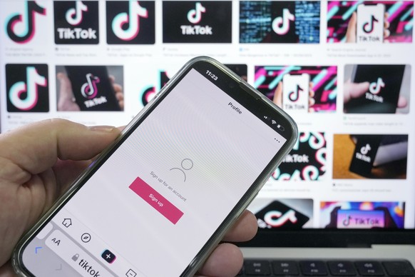 A sign up page for the application TikTok is shown on a cell phone in front of a screen with logos for the company in Sydney, Tuesday, April 4, 2023. Australia had become the last of the Five Eyes sec ...