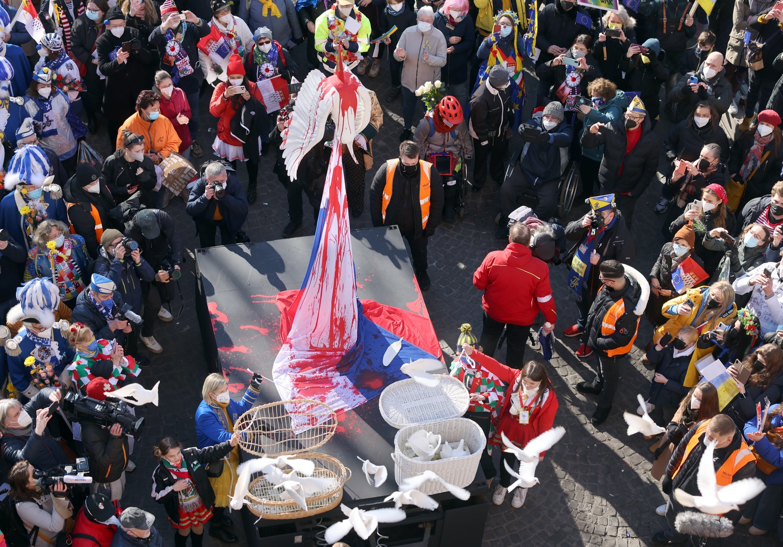 28.02.2022, Nordrhein-Westfalen, K�ln: Wei�e Tauben werden bei der Kundgebung zur Friedensdemonstration am Rosenmontag in die Freiheit entlassen. Dahinter ist eine auf einer russischen Fahne scheinbar ...