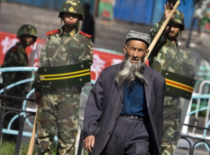 Ein Angehöriger der uigurischen Minderheit in China geht in Ürümqi in der Region Xinjiang in Nordwestchina vorbei an chinesischen Sicherheitskräften.