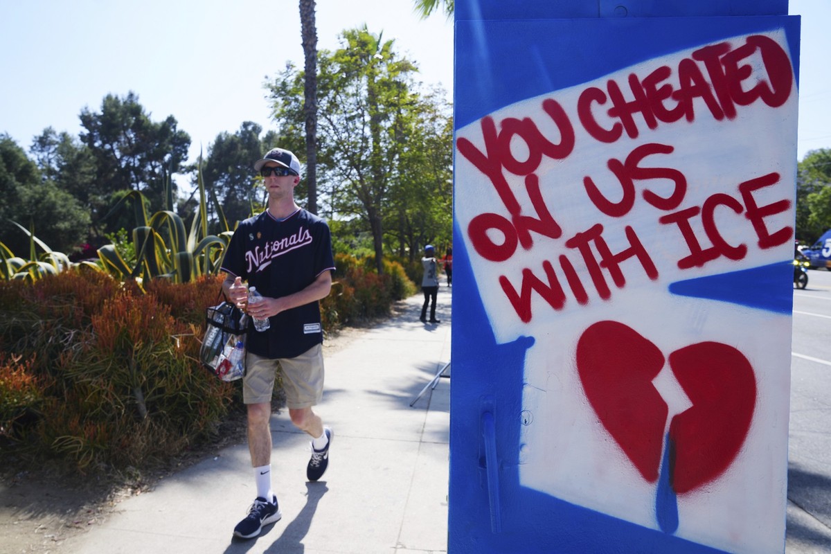 21.06.2025, USA, Los Angeles: Ein Fan geht bei seiner Ankunft zu einem Spiel zwischen den Los Angeles Dodgers und den Washington Nationals an einem Schild mit der Aufschrift «You cheated us with ICE»  ...