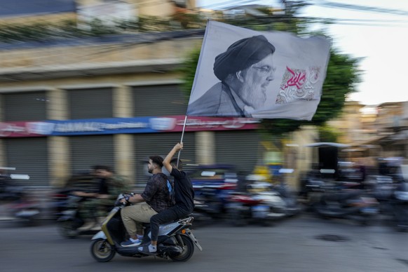 Hezbollah supporters carry a flag depicting Hezbollah leader Hassan Nasrallah as they ride a scooter following the funeral procession of Hezbollah commanders Ibrahim Kobeisi and Hussein Ezzedine in Be ...