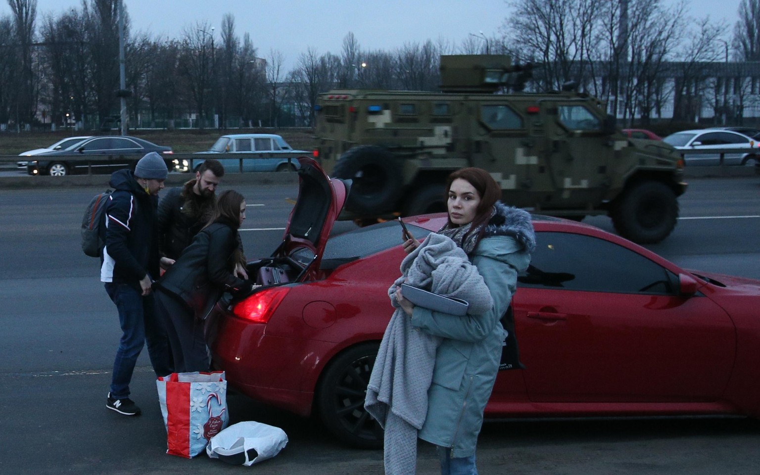 8124772 24.02.2022 People load their stuff into a car as a military vehicle drives past on a street in Kiev, Ukraine. On February 24 Russian President Vladimir Putin announced a military operation in  ...