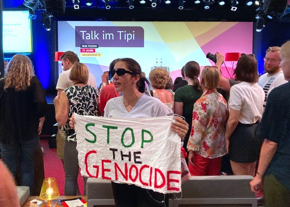 26.05.2024, Berlin: &quot;Stop the Genocide&quot; steht auf einem Transparent, dass eine Frau während einer Veranstaltung mit Außenministerin Baerbock im Rahmen der Demokratiefestets anlässlich des Ju ...