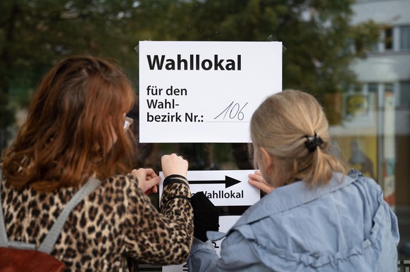 Wahlhelferinnen hängen einen Zettel mit der Aufschrift "Wahllokal für den Wahlbezirk Nr.: 102" an einem Wahllokal auf. Am 26. September findet die Bundestagswahl 2021 statt.