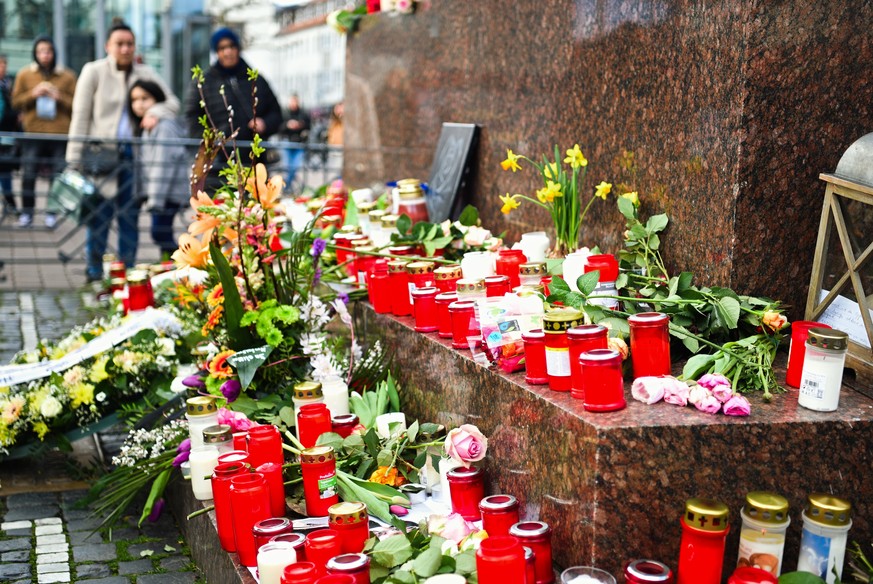 Menschen stehen um das Brüder-Grimm-Denkmal in Hanau, an dem Blumen und Kerzen niedergelegt worden sind.