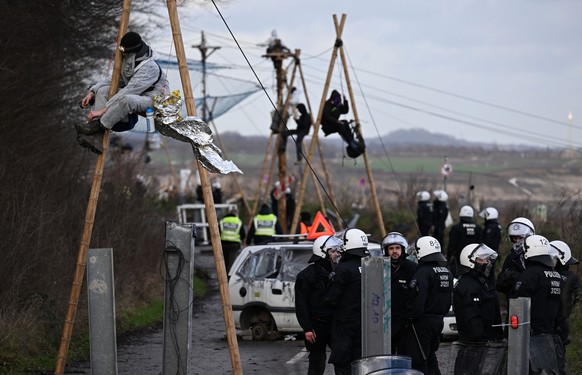 11.01.2023, Nordrhein-Westfalen, Erkelenz: Demonstranten sitzten während der Räumung des Dorfes Lützerath auf Konstruktionen aus Balken. Der Energiekonzern RWE will die unter Lützerath liegende Kohle  ...