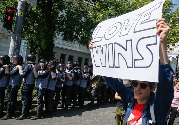 epaselect epa05358747 A participant carries a placard as policemen guard participants of the gay pride parade in downtown Kiev, Ukraine, 12 June 2016. Representatives of LGBT (Lesbian, Gay, Bisexual a ...