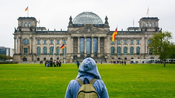 Young woman with backpack looking at Bundestag building in Berlin. Erasmus student, studying abroad and tourist concept.