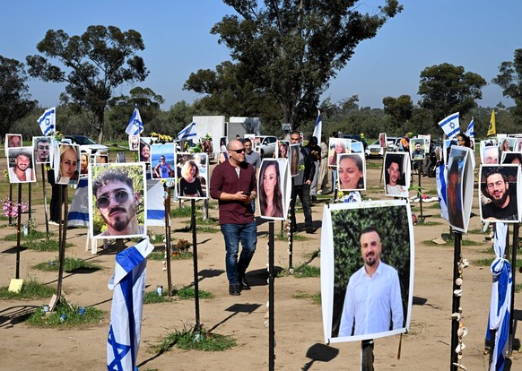 People walk by national flags and portraits of Israelis taken captive or killed by Hamas militants during the October 7 attacks, at the site of the Supernova Music Festival in Reim on Saturday, Januar ...