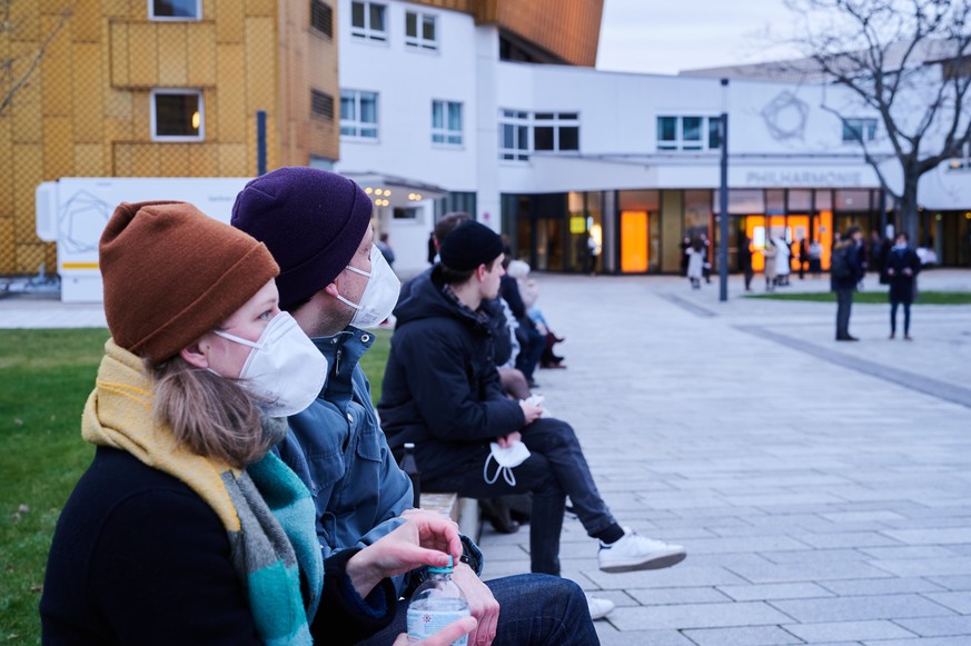 20.03.2021, Berlin: Besucher mit FFP2-Masken sitzen vor der Berliner Philharmonie und warten noch auf die Ergebnisse ihrer Tests auf das Coronavirus. In dem Konzerthaus findet am Abend ein Testkonzert ...