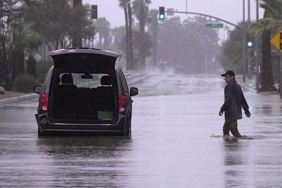 A motorist walks out to remove belongings from his vehicle after becoming stuck in a flooded street, Sunday, Aug. 20, 2023, in Palm Desert, Calif. Forecasters said Tropical Storm Hilary was the first  ...